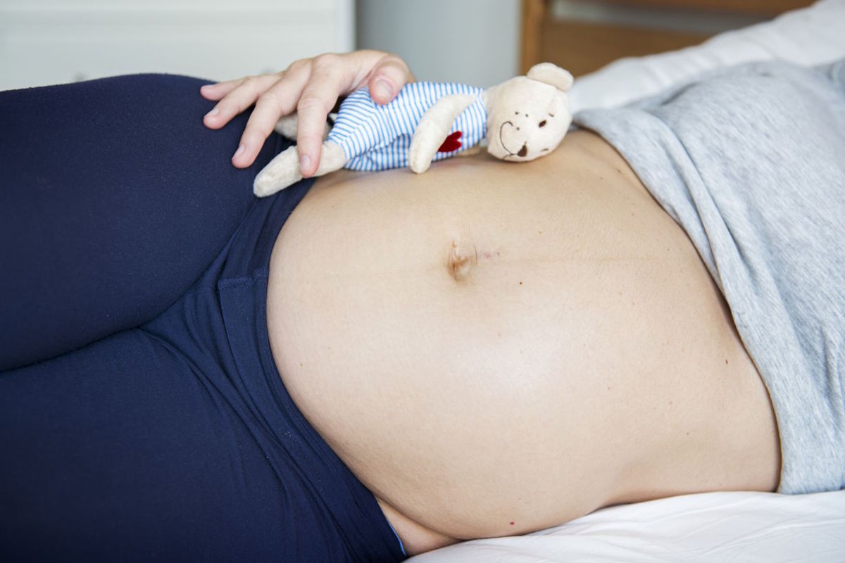 Schwangere Frau liegt im Bett, mit einem Kuscheltier auf dem Bauch | Basic Bonding in der Schwangerschaft